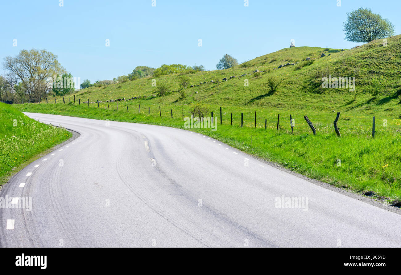 Country road through scenic hill landscape. Person sitting on rock in far distance, looking out over the vista. Location Brosarp in Scania, Sweden. Stock Photo