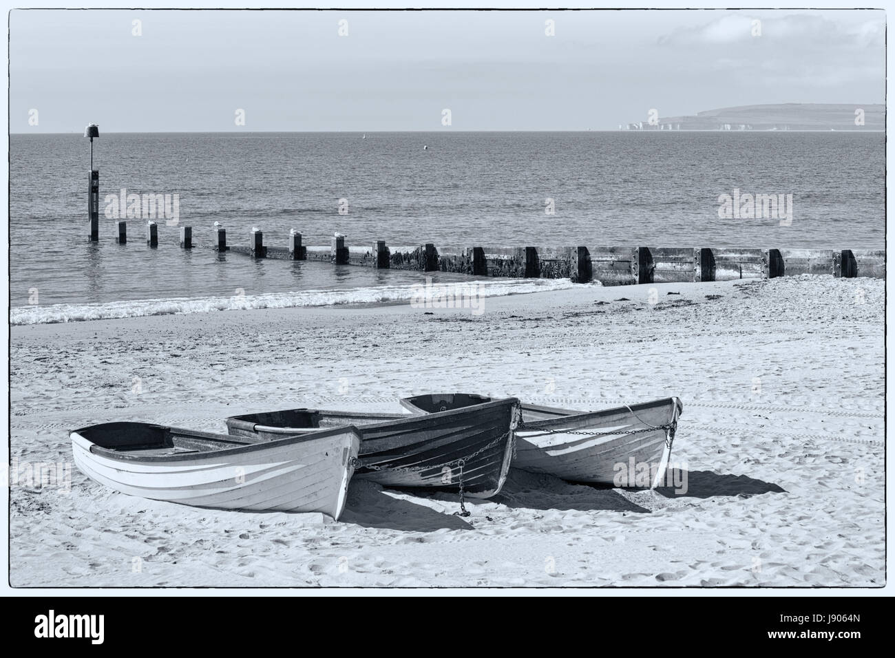 Fishing boats on sand at Durley Chine beach, Bournemouth, Dorset in May - fine art monochrome black and white Stock Photo