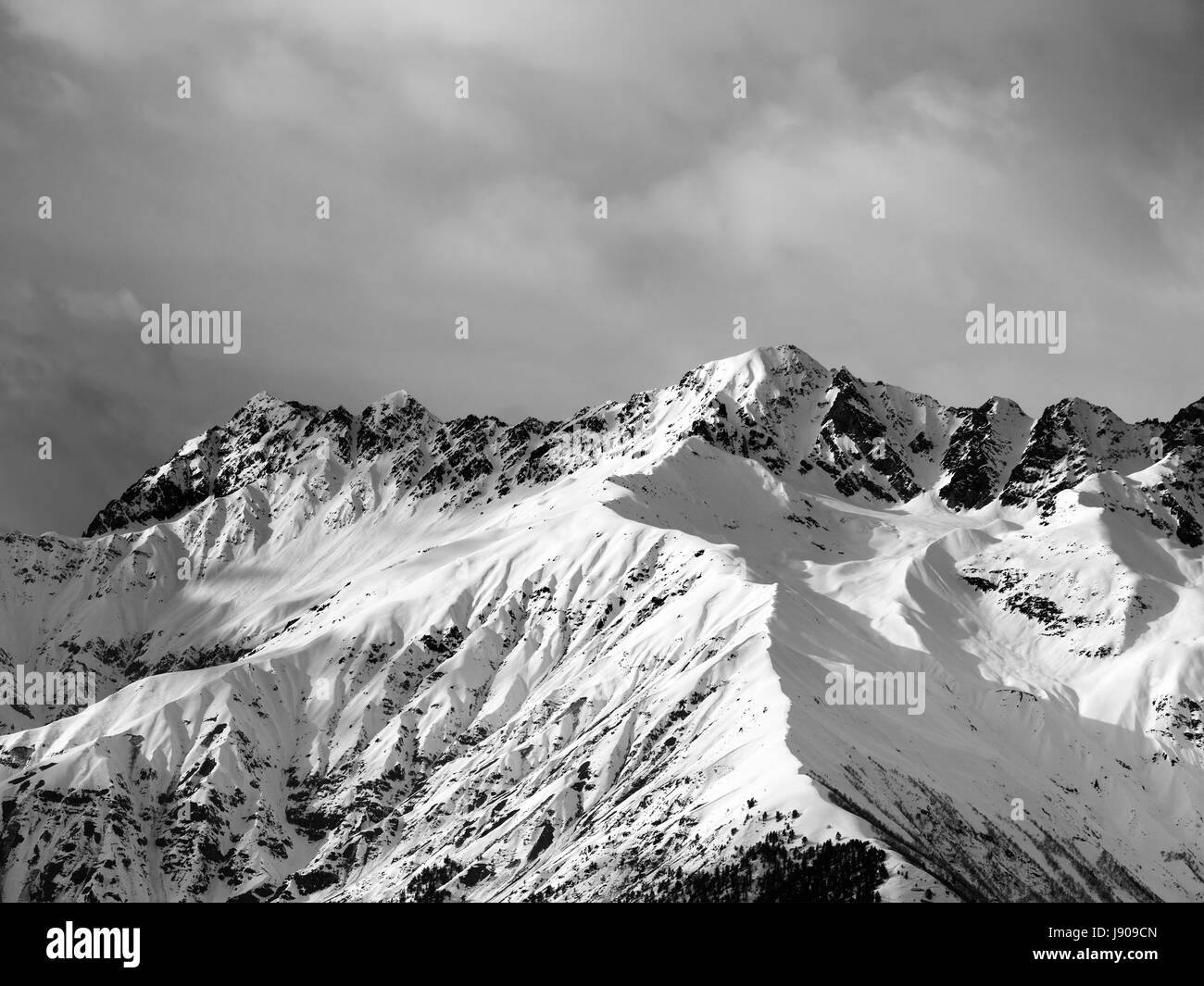 Black and white view on snow sunlight mountain and cloudy sky at winter evening. Caucasus Mountains. Svaneti region of Georgia. Stock Photo