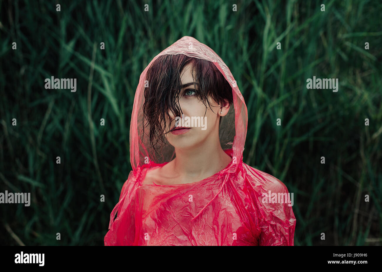 The portrait of girl in red raincoat under the rain. Sad and serious