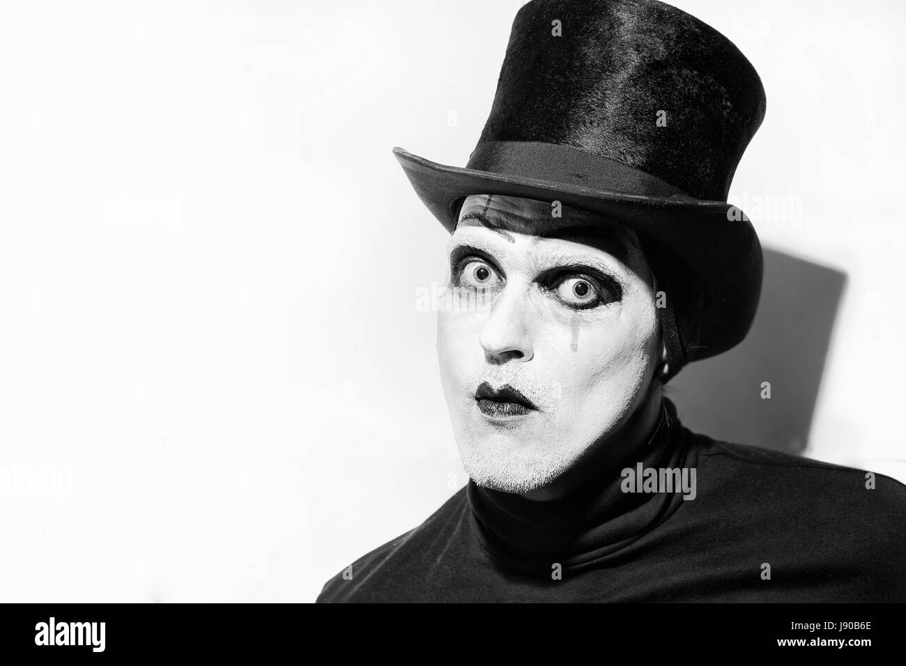 Portrait of a scary angry mime wearing a tall hat on white background.  Theatrical make-up Stock Photo