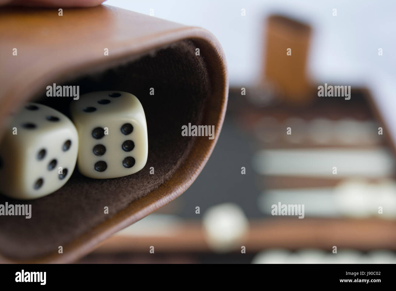 Readying to roll backgammon dice on the brown and cream backgammon board blurred in the background. Focusing on the dice in the dice cup. Stock Photo