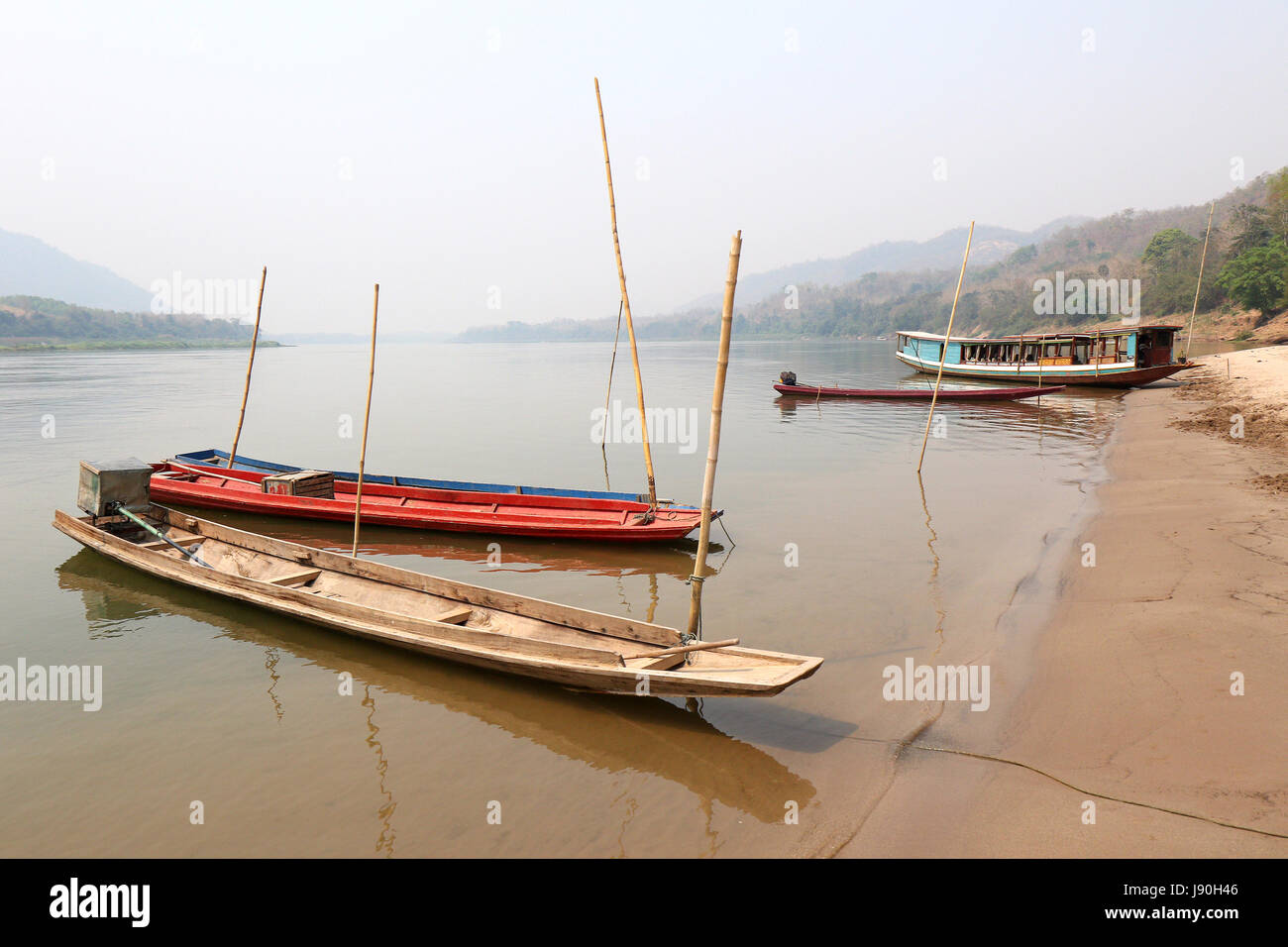 Boats on Laos beach on the Mekong, by a Luang Prabang fishing village. Haze  on the horizon is due to forest clearance fires set by farmers Stock Photo  - Alamy