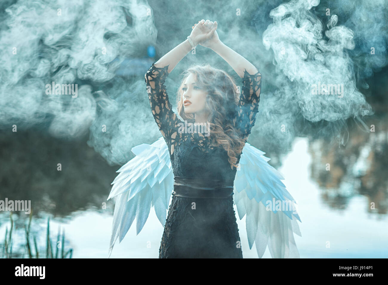 Girl with angel wings is shrouded in smoke. This occurs in the open air on a river. Stock Photo