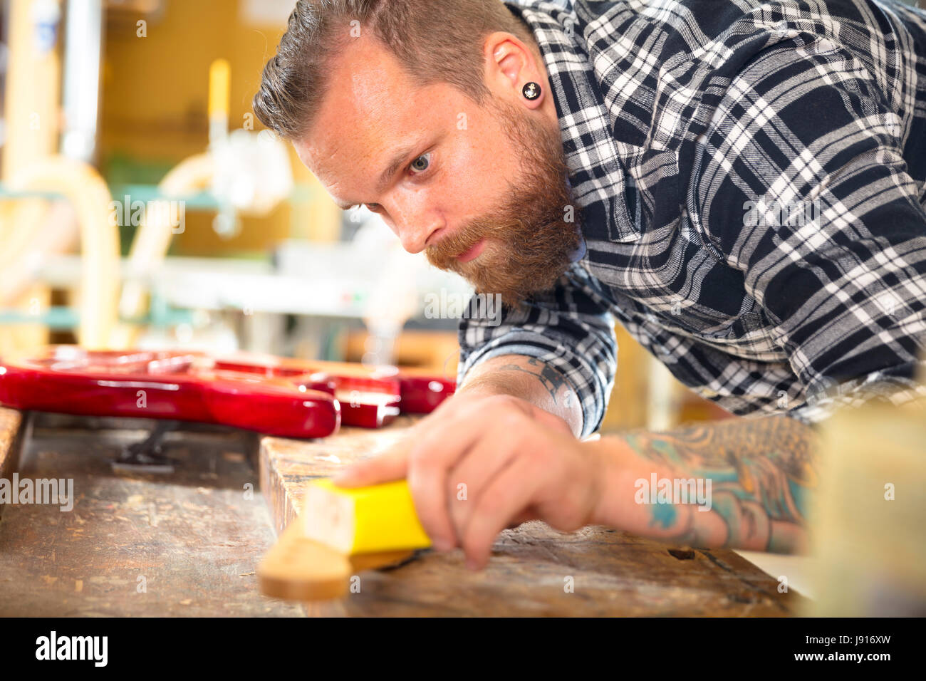 Carpenter sanding guitar neck in wood at workshop Stock Photo