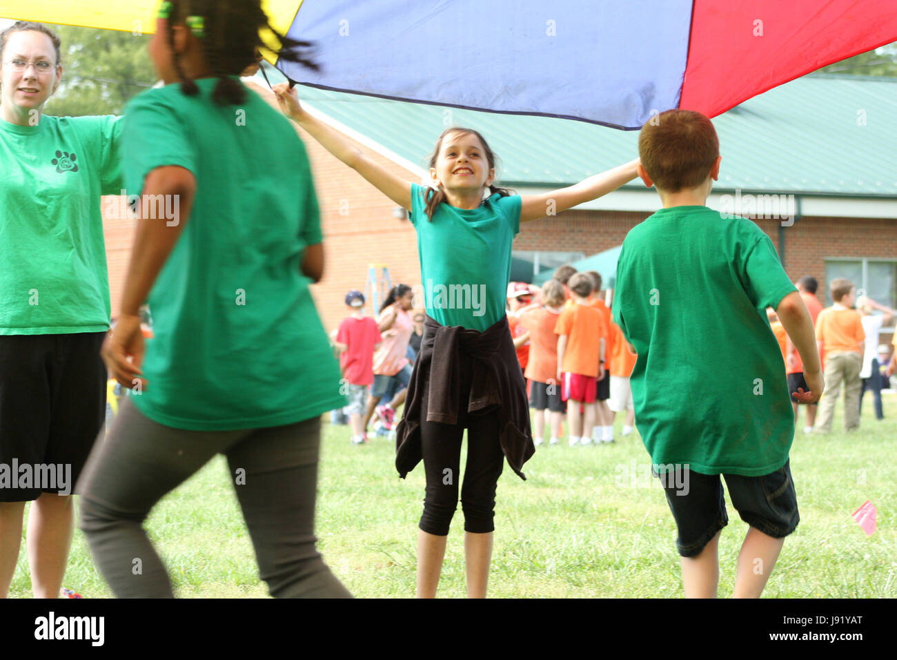 School students and teacher playing with large parachute during recess