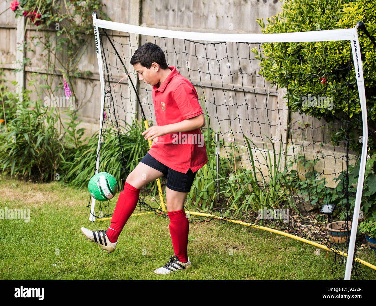 Boy plays football in garden, with goal net Stock Photo