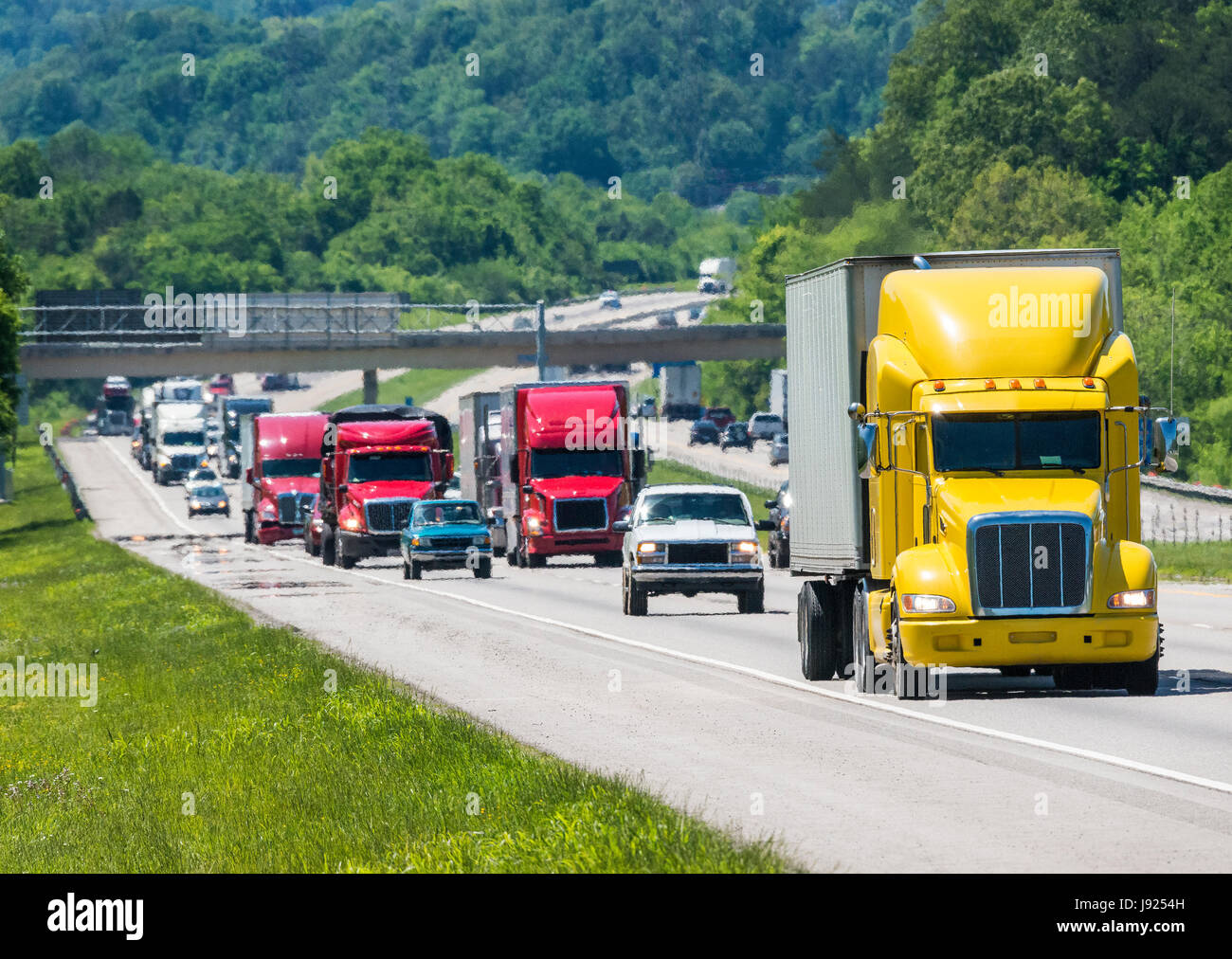 A yellow semi leads a packed line of traffic down an interstate in Tennessee.  Heat rising from the pavement gives a shimmering effect to vehicles and Stock Photo