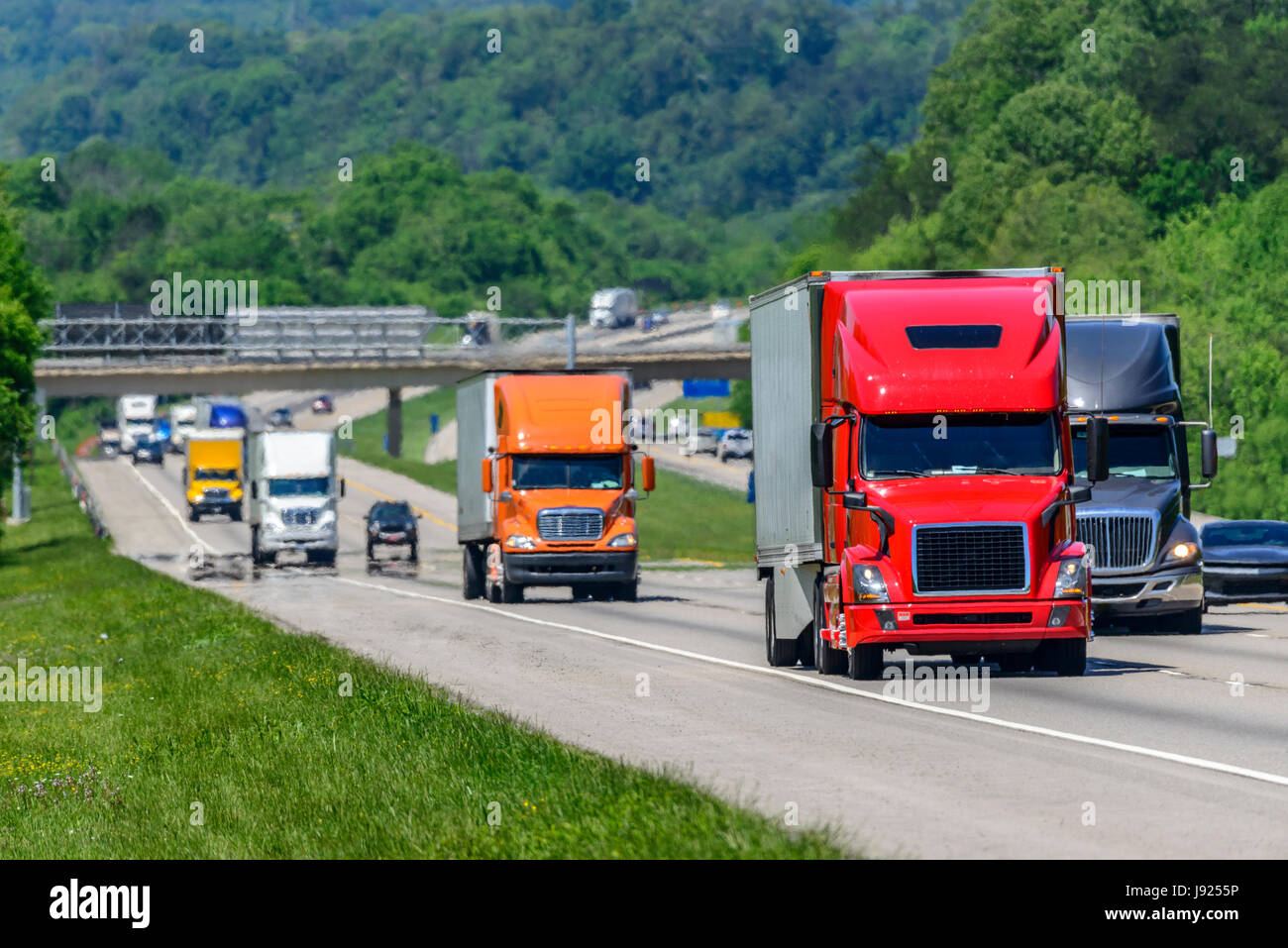 A steady flow of semis lead the way down a busy interstate highway in Tennessee.  Heat waves rising from the pavement give a nice shimmering effect to Stock Photo