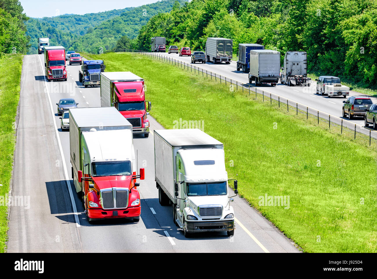 A heavy flow of 18-wheelers peppered with cars and SUVs roll down a Tennessee interstate highway.  Heat rising from the pavement gives a shimmering ef Stock Photo