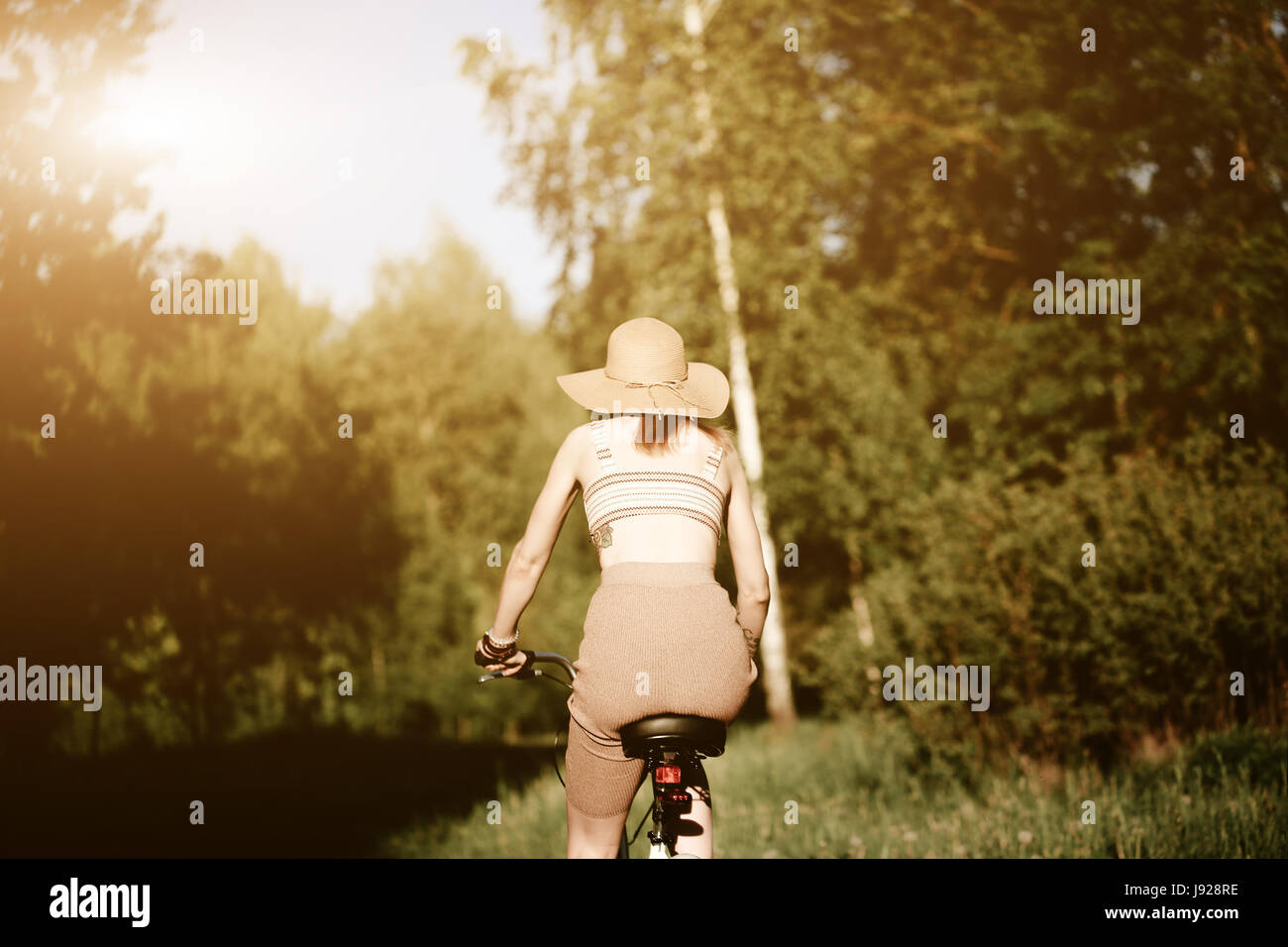 Funny girl driving bicycle outdoor. Sunny summer lifestyle concept. Woman in dress and hat in Field with dandelions. Female ride in park. Light photo  Stock Photo
