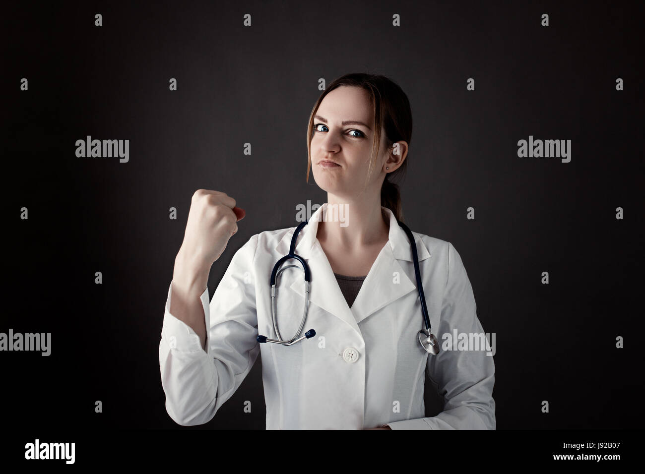 Female Intern Holds a fist and look in camera with strong face. Stethoscope or phonendoscope on neck. Medicine photo. Medical care or insurance concep Stock Photo