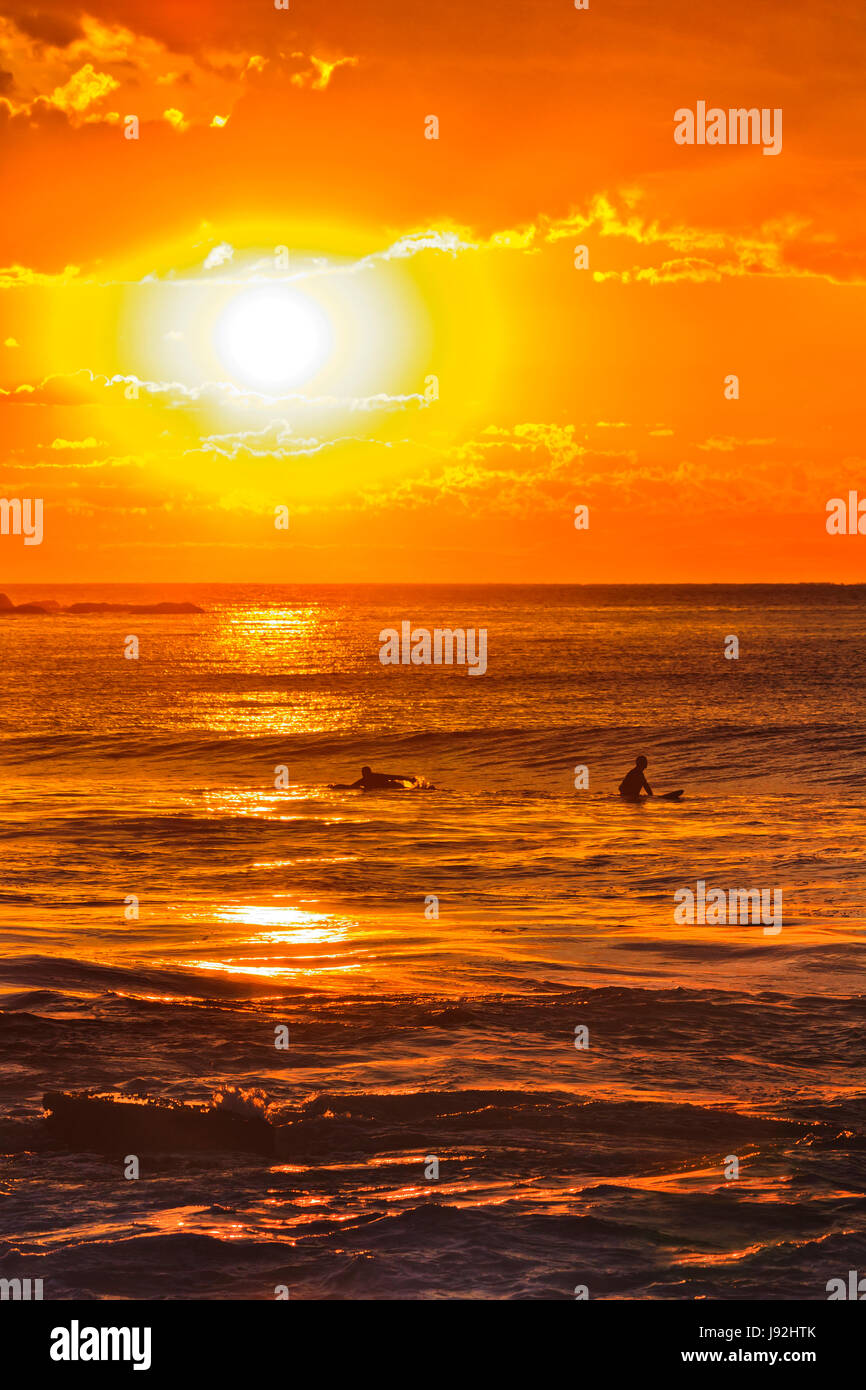 Colourful orange sunrise over sea horizon with surfers floating and waiting to ride a wave off Avalon beach in Sydney, Australia. Stock Photo