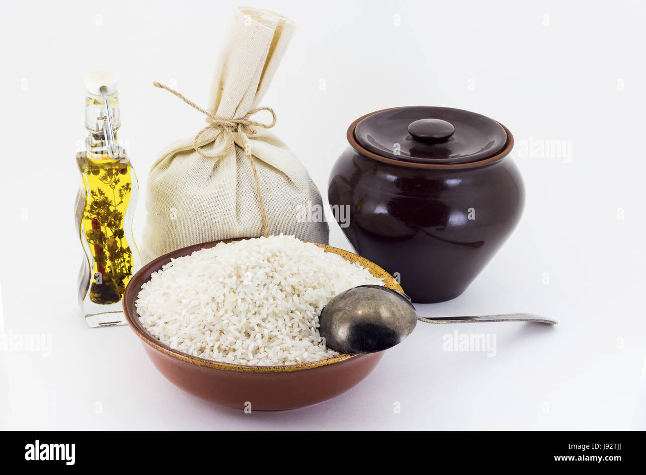 Still life of Rice cereal in ceramic pial, ceramic pot, old spoon and canvas bag for cereals, oil with spices and seasonings, isolated on white backgr Stock Photo