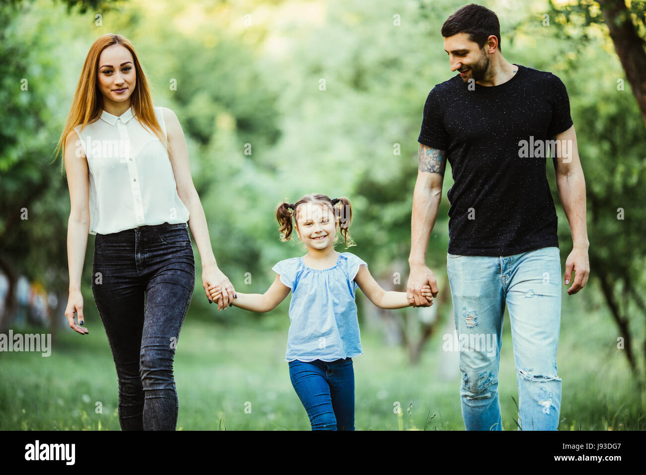 family, parenthood, adoption and people concept - happy mother, father and little girl walking in summer park Stock Photo