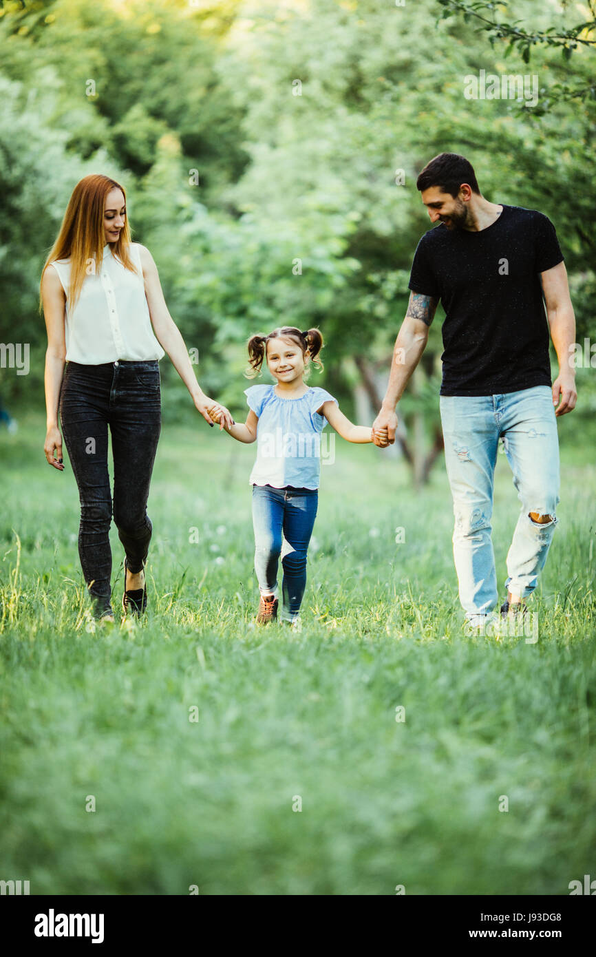 family, parenthood, adoption and people concept - happy mother, father and little girl walking in summer park Stock Photo