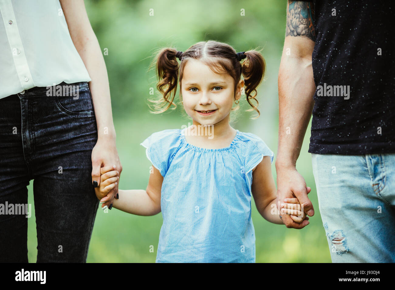 Excited young girl holding hands while walking with parents in park Stock Photo