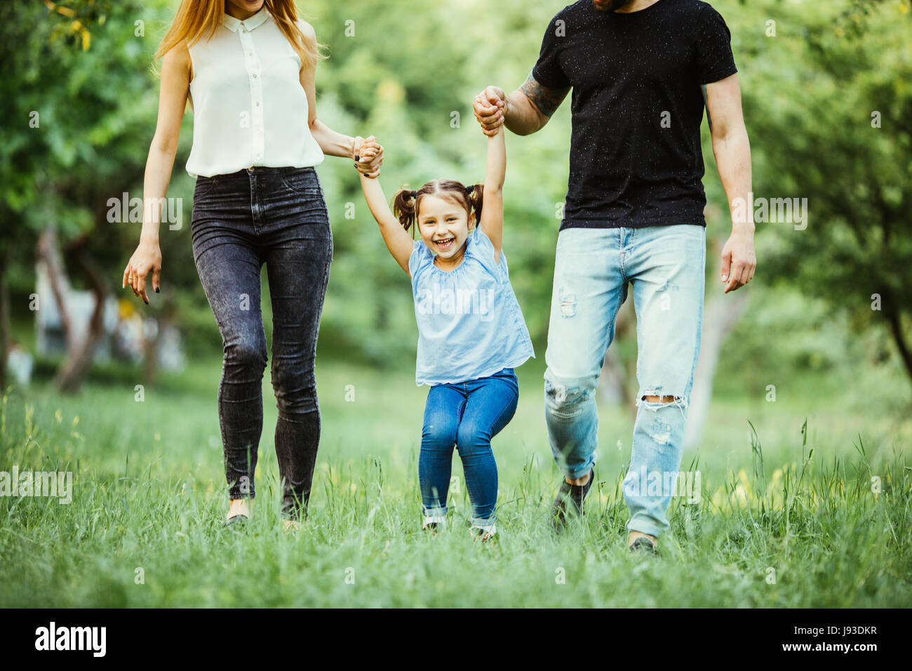 Excited young girl holding hands while walking with parents in park Stock Photo