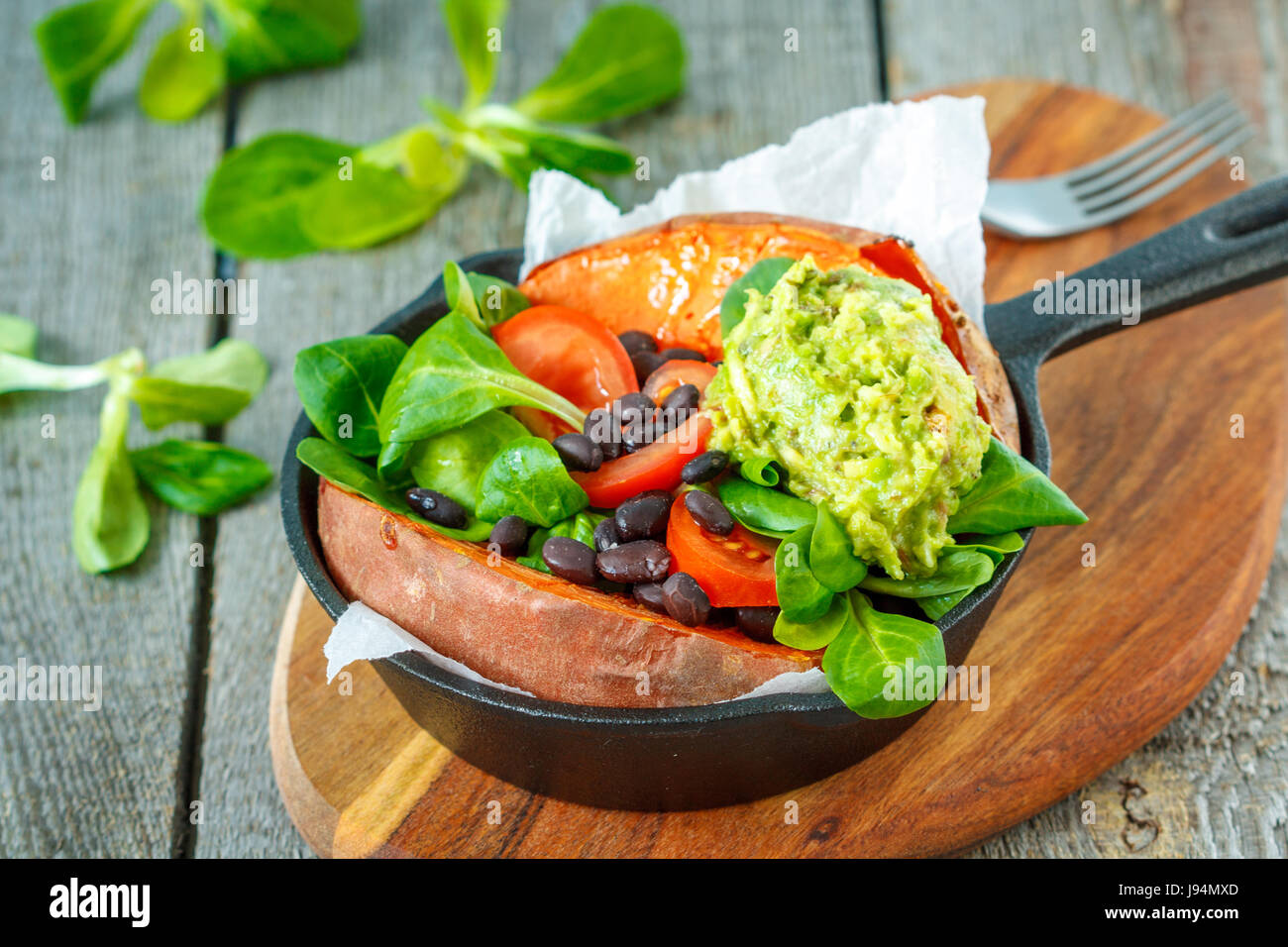 Baked whole sweet potato with guacamole and black beans in a castiron