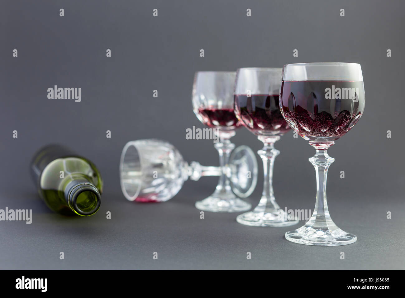 Concept of alcohol consumption, alcoholism and abuse with a line of beautiful crystal glasses filled with red wine and an empty bottle. Stock Photo