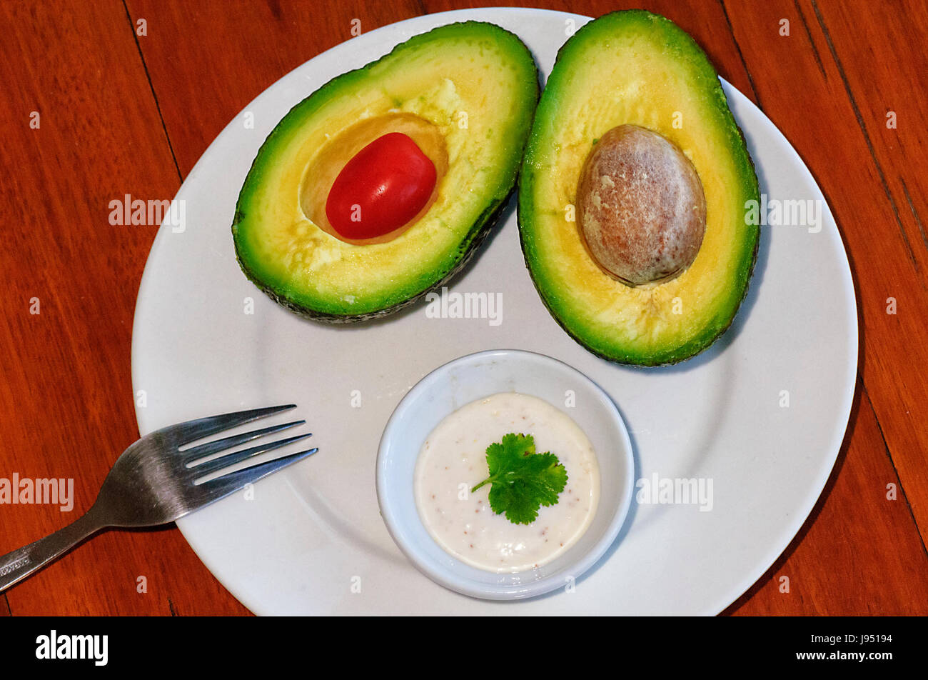 Avocado pear cut in two halves, with tomato and Aioli Sauce Stock Photo