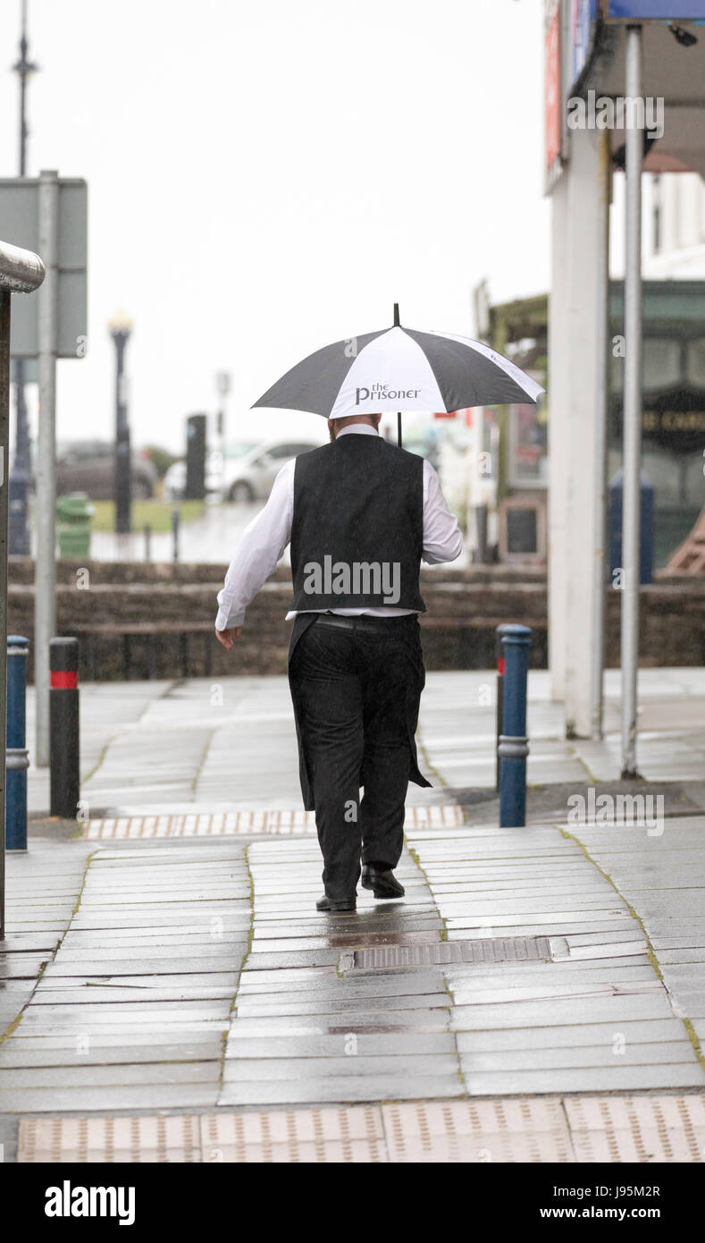 A waither caught out in the rain as he makes his way to work under an umbrella to serve in one mainy tea rooms at the populars seasdide town of Llandudno, Wales, UK Stock Photo