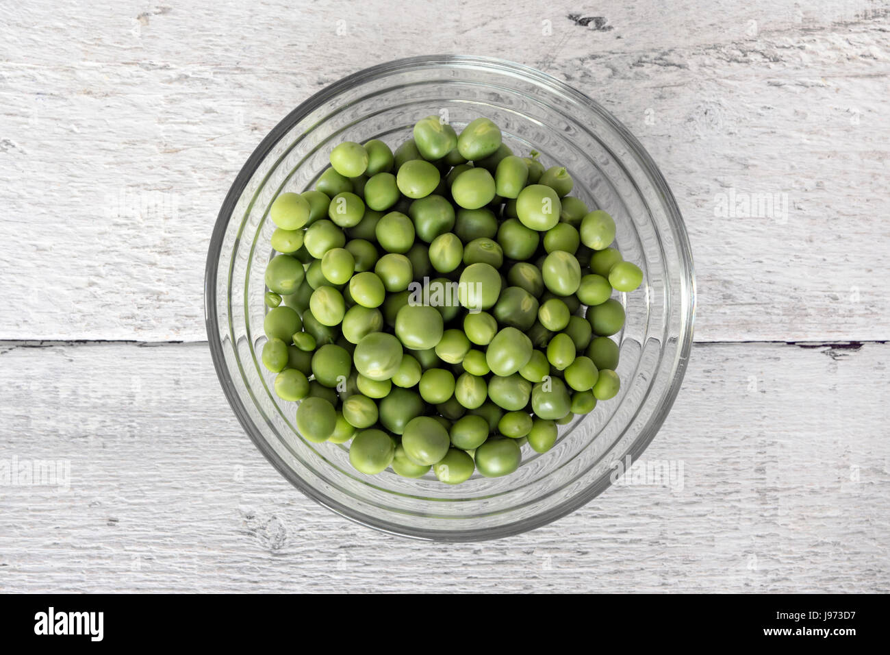 Green peas, freshly picked, in a glass bowl, on white wooden table. Top view Stock Photo