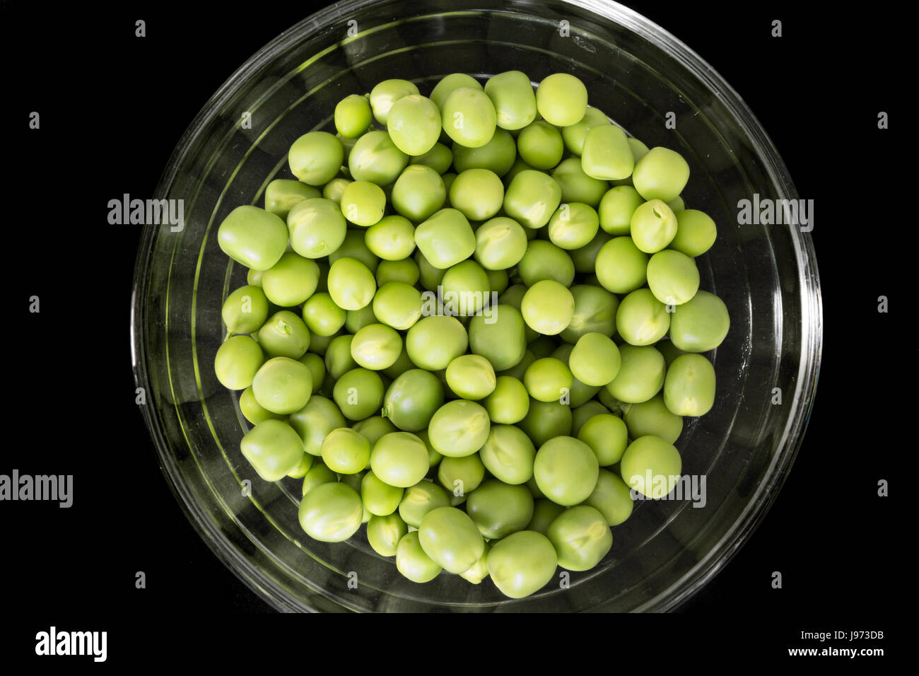 Green peas, freshly picked, in a glass bowl, on black background. Top view Stock Photo