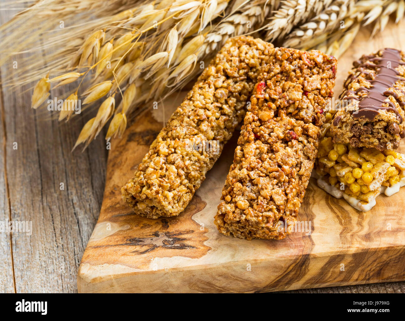 Healthy granola cereal bars with wheat ears on wooden board Stock Photo