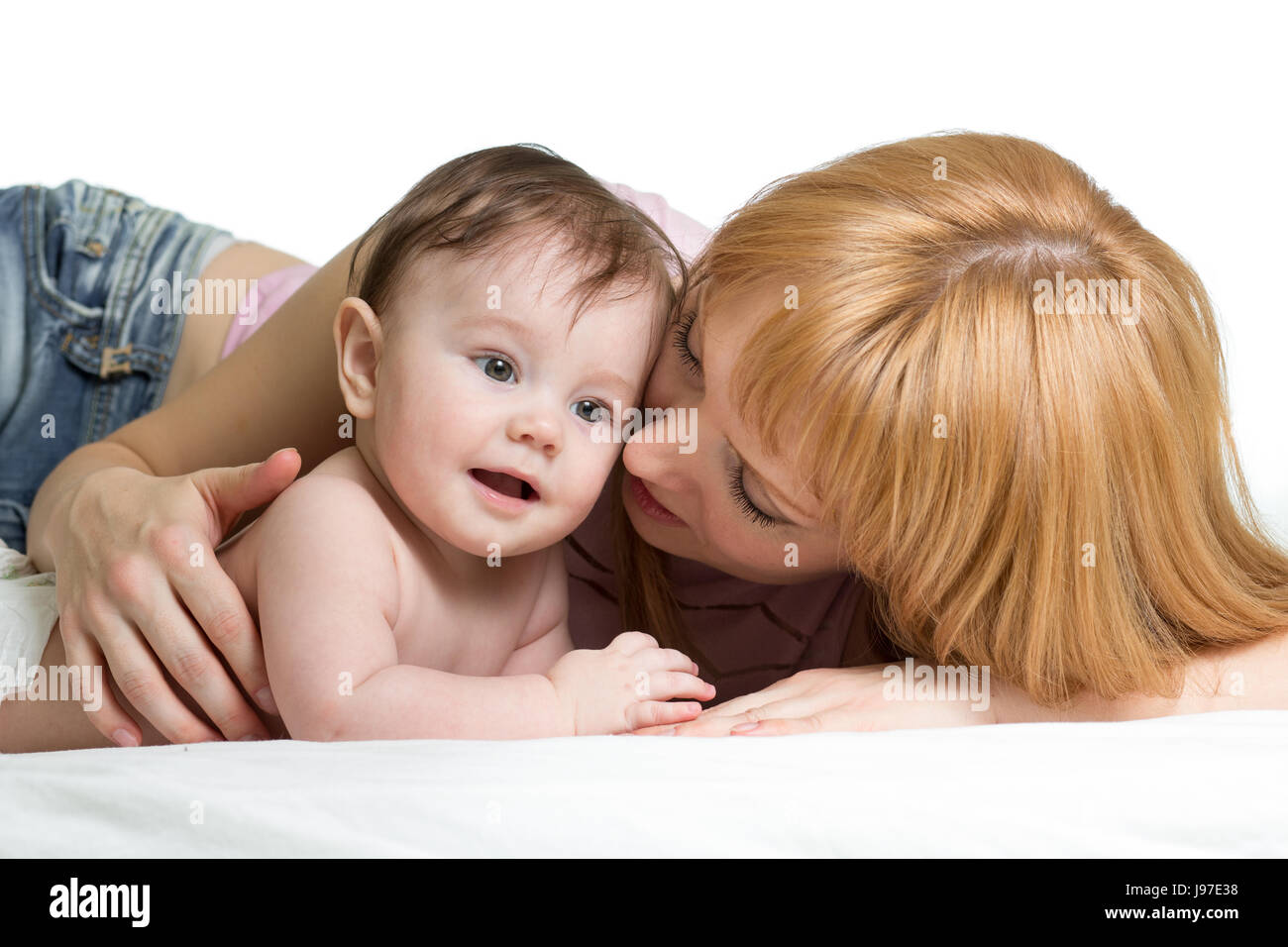 Cute mother embraces her little baby. Woman and newborn kid boy relax in a white bedroom. Stock Photo