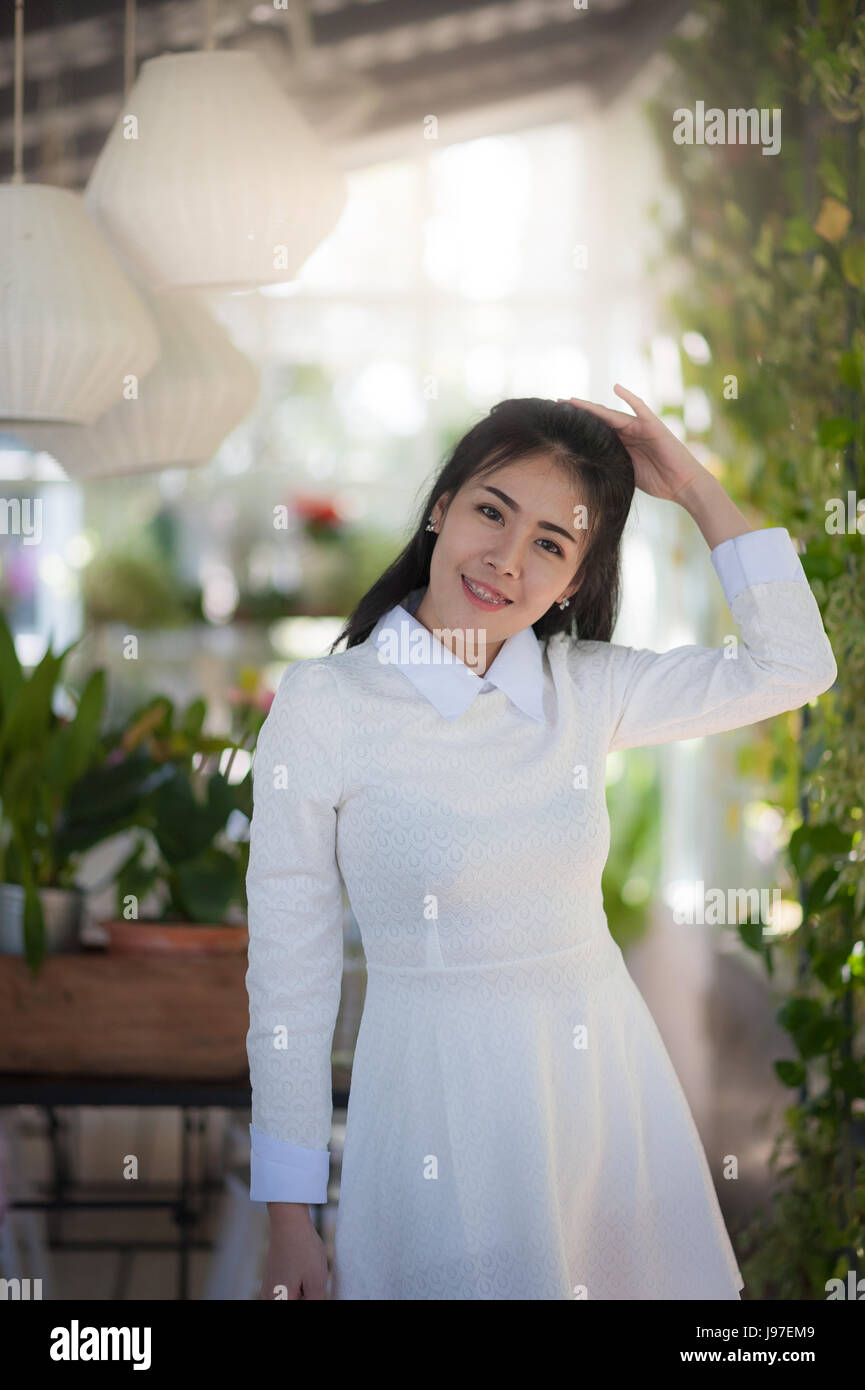 Young attractive Asian woman wear white vintage cloths smiling in green garden. Stock Photo