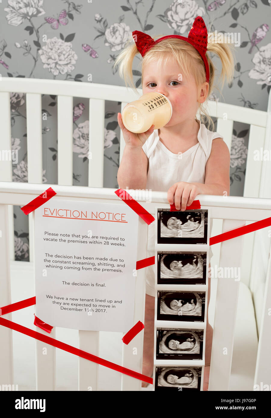 Funny baby announcement. A child stood up in the cot with a funny eviction notice on side. Stock Photo