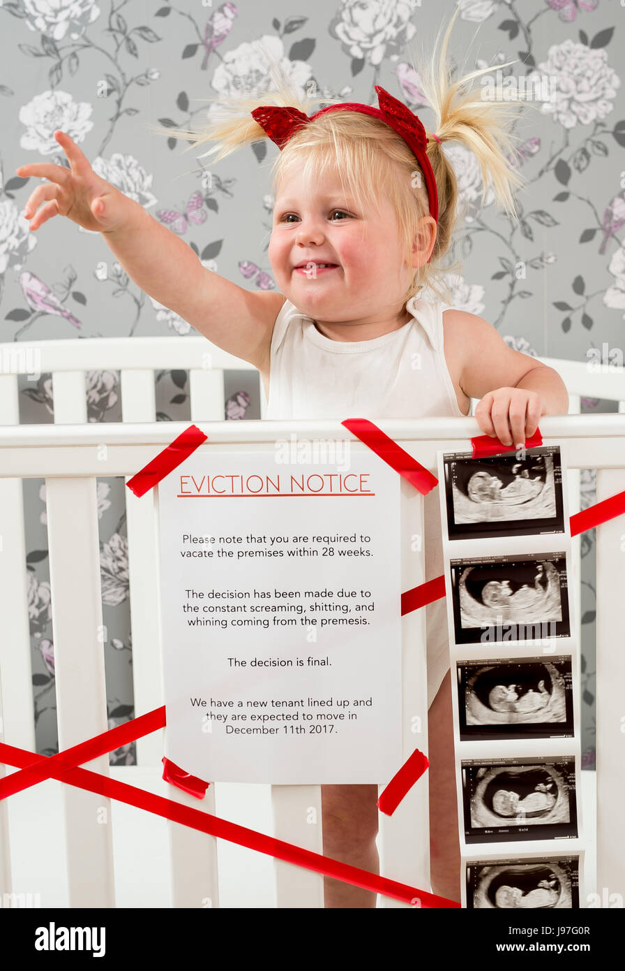 Funny baby announcement. A child stood up in the cot with a funny eviction notice on side. Stock Photo