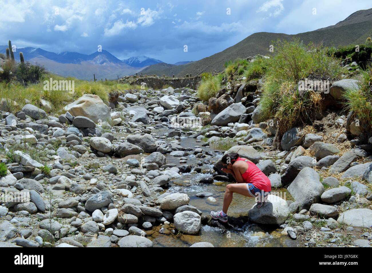 Woman athlete calms his thirst in a crystalline brook of the heights of the valley of the snowfall of Cachi, Salta, Argentina Stock Photo
