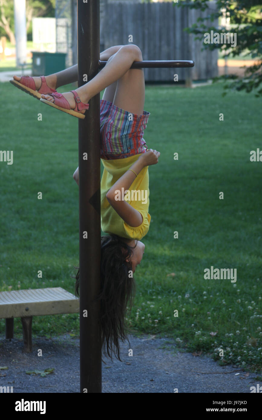 Young girl hanging upside down from exercise bars in park Stock Photo