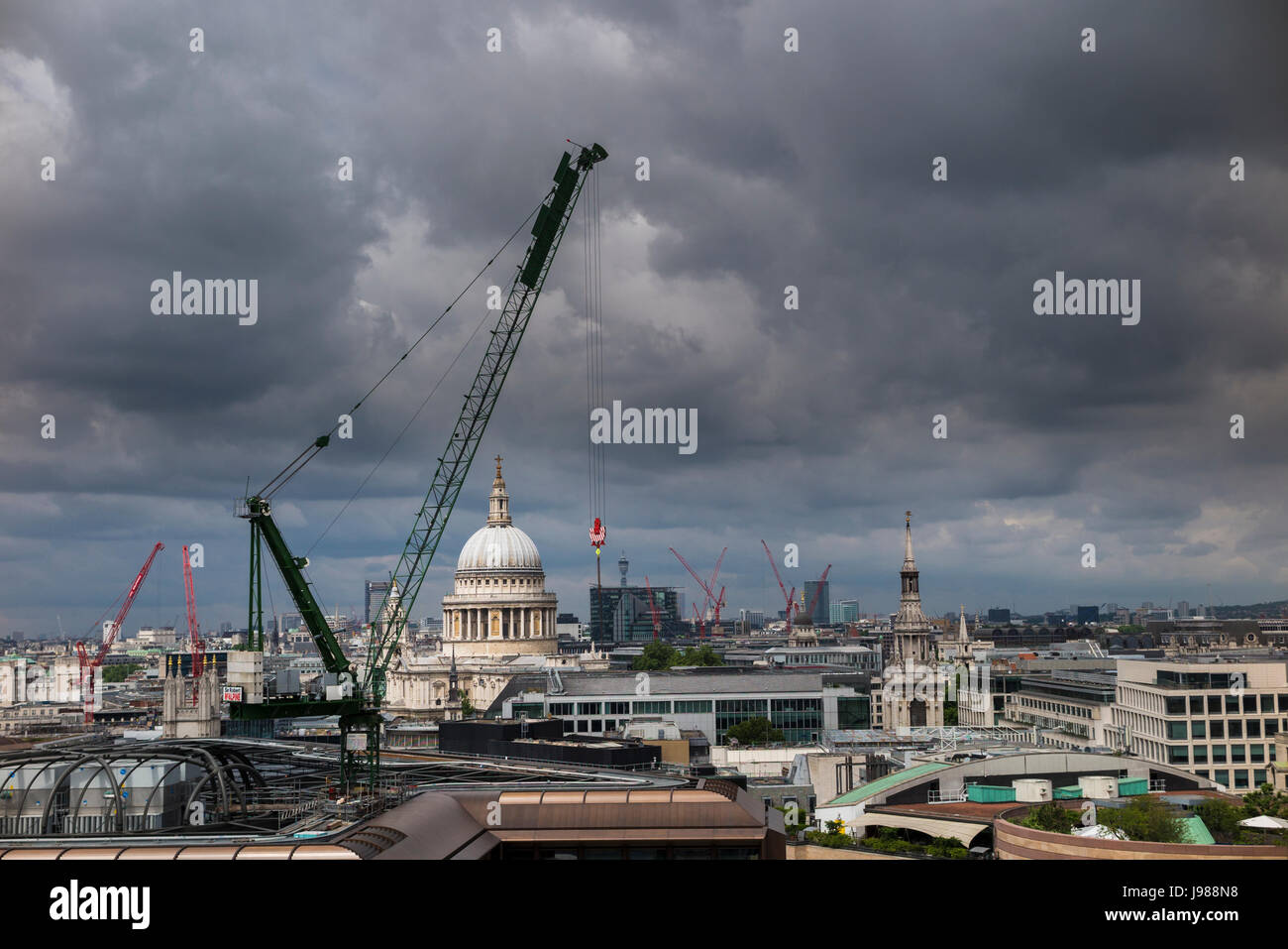 Tower cranes at the Bloomberg Place development site on the City of London skyline overlooking St Paul's Cathedral with grey gathering clouds Stock Photo