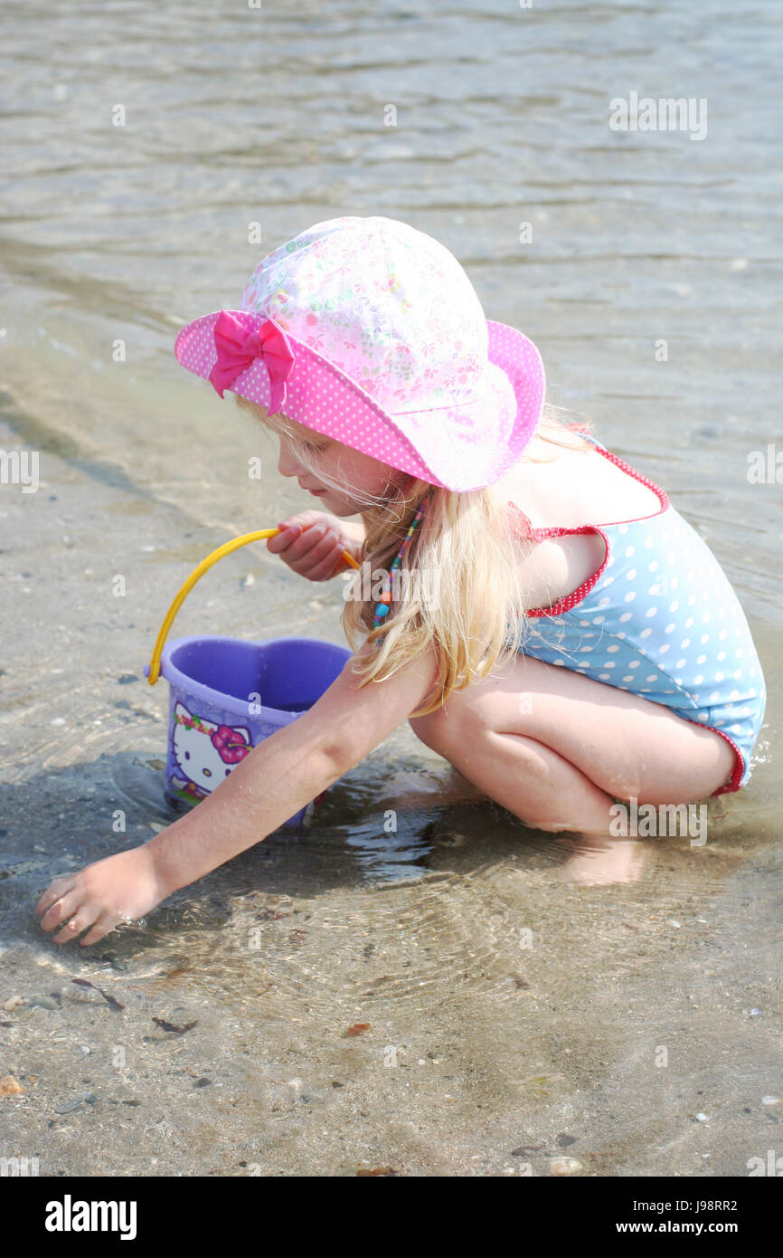 Little girl, child collecting shells at the beach with a bucket wearing