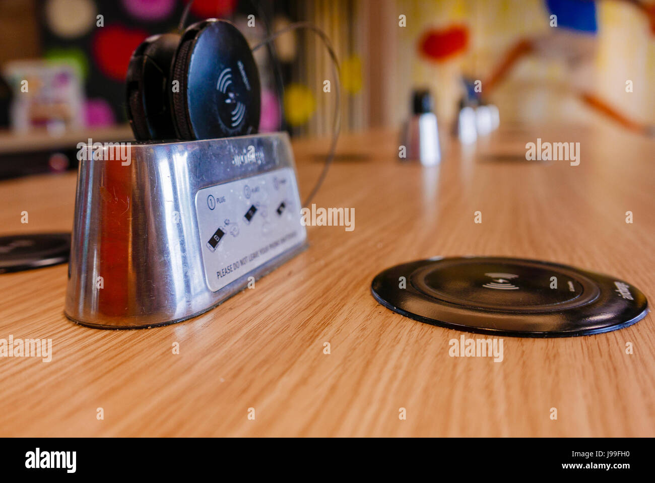 QI wireless chargers built into a table at a McDonald's restaurant, with wireless receiver adapters for devices without wireless capability Stock Photo