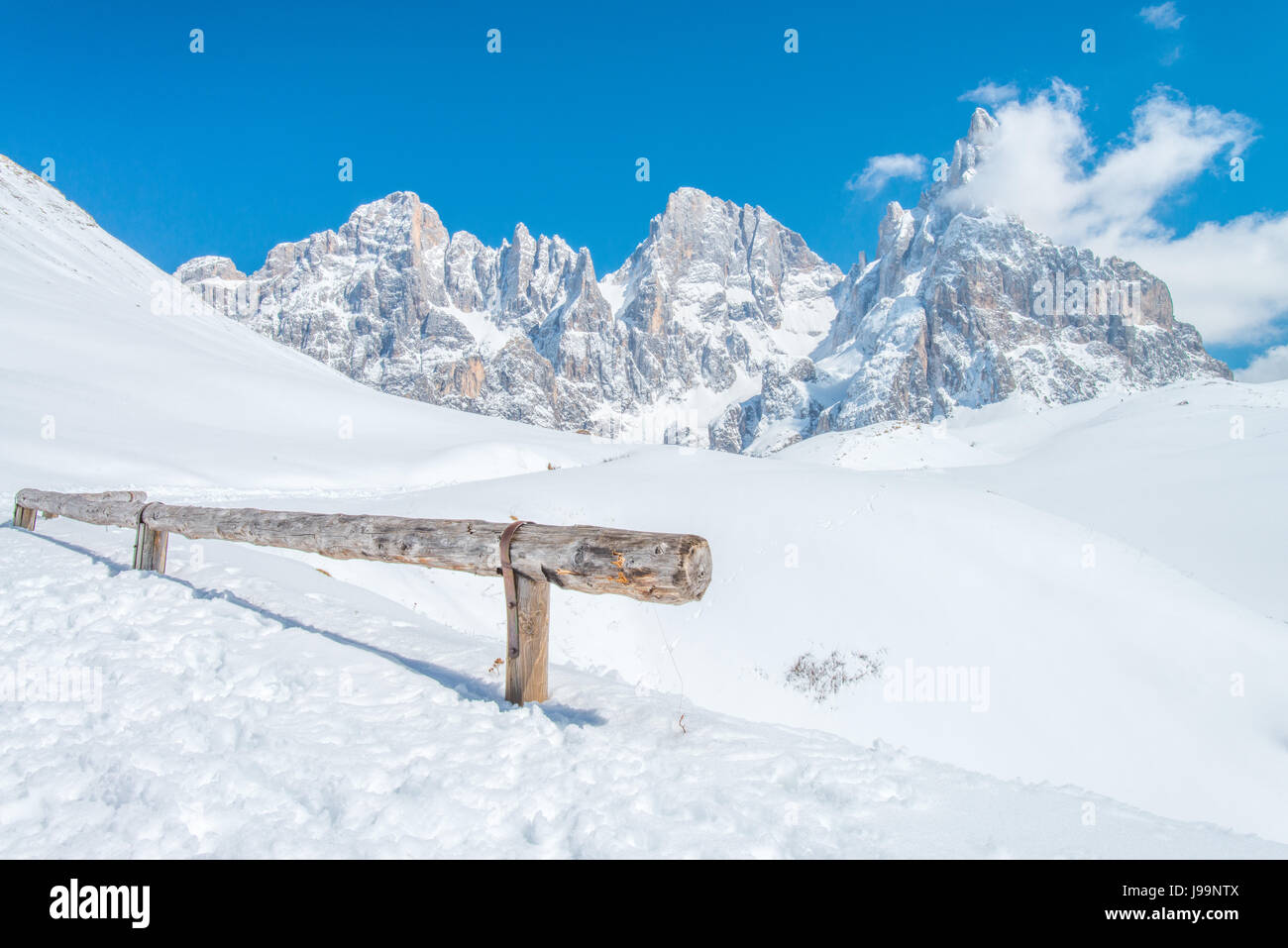 An old wooden log, fence stays in the foreground to some amazing, rugged mountains in the Italian Dolomites - Fresh powder on the trail Stock Photo