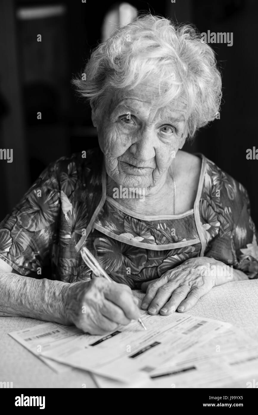 Elderly woman fills a receipt for the utilities. Black-and-white photo. Stock Photo