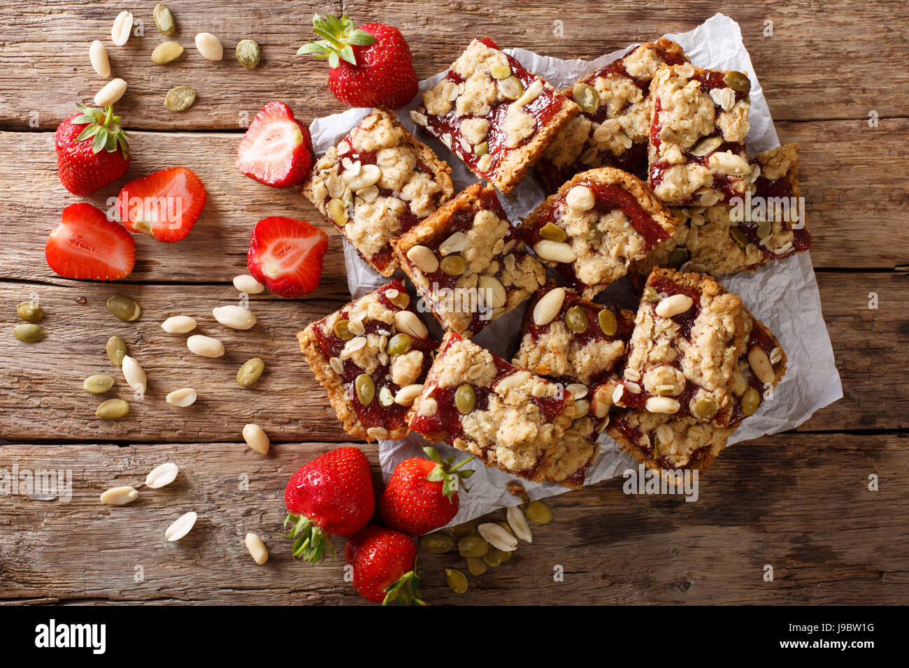 Homemade strawberry bars with oatmeal, peanuts and pumpkin seeds close-up on the table. horizontal view from above Stock Photo