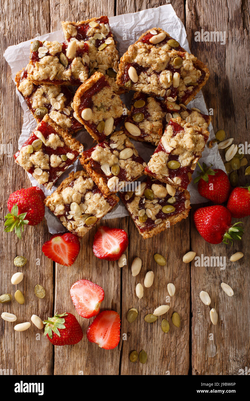 Homemade strawberry bars with oatmeal, peanuts and pumpkin seeds close-up on the table. vertical view from above Stock Photo