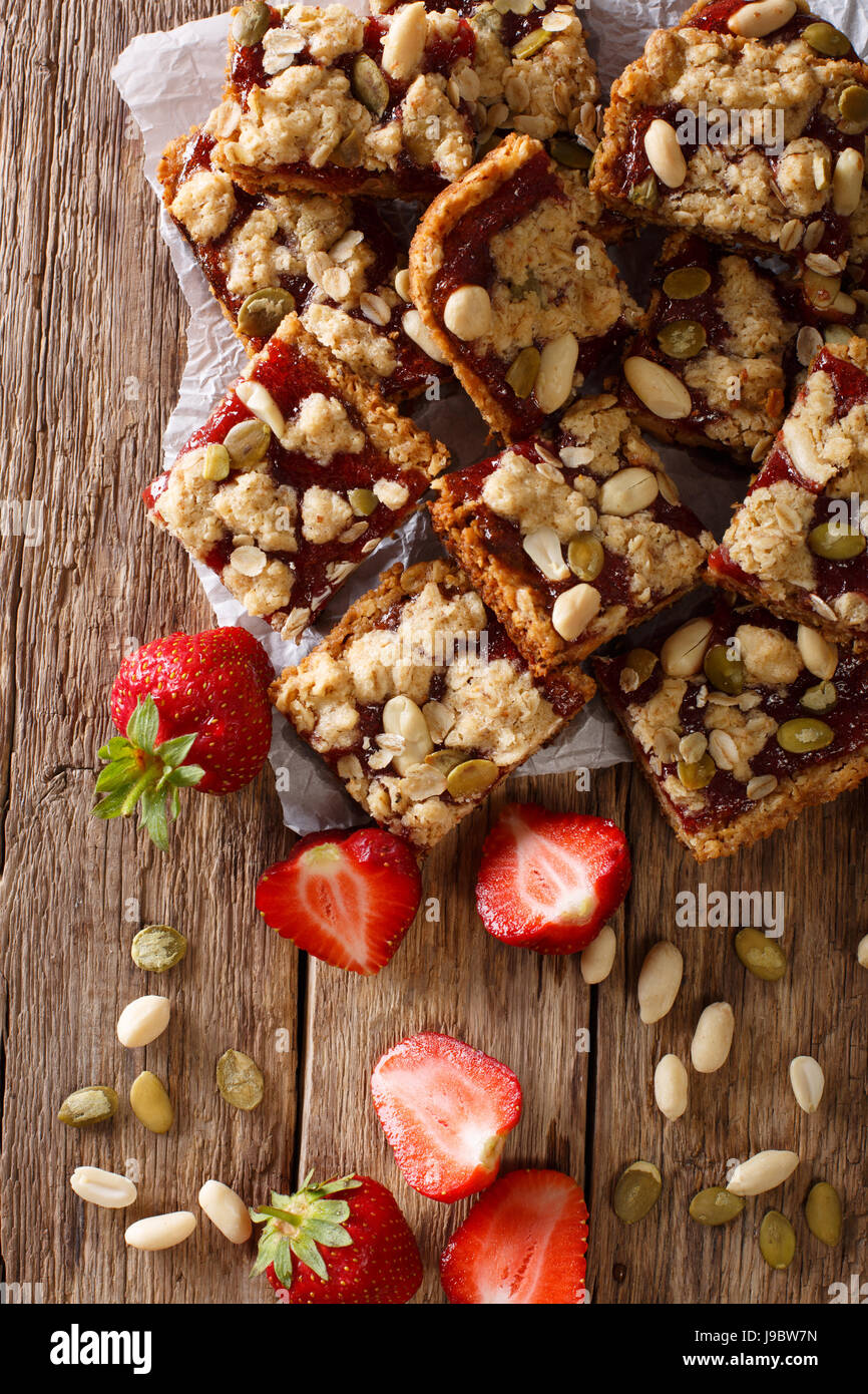 Oat bars with strawberries, seeds and nuts close-up on the table. Vertical view from above Stock Photo