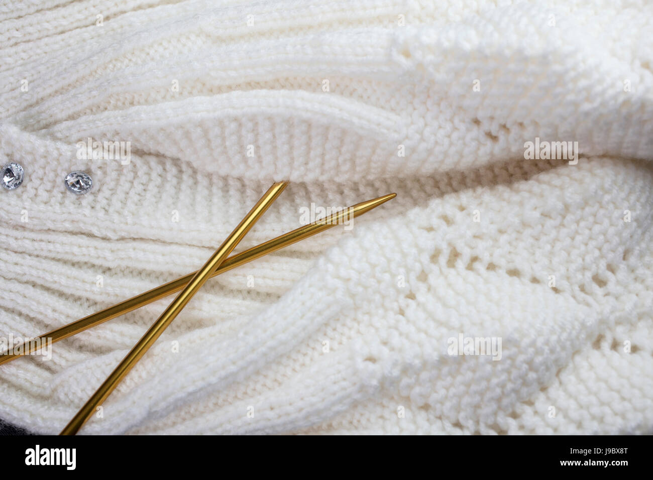 White yarn knitted garment with gold colored knitting needles Stock Photo