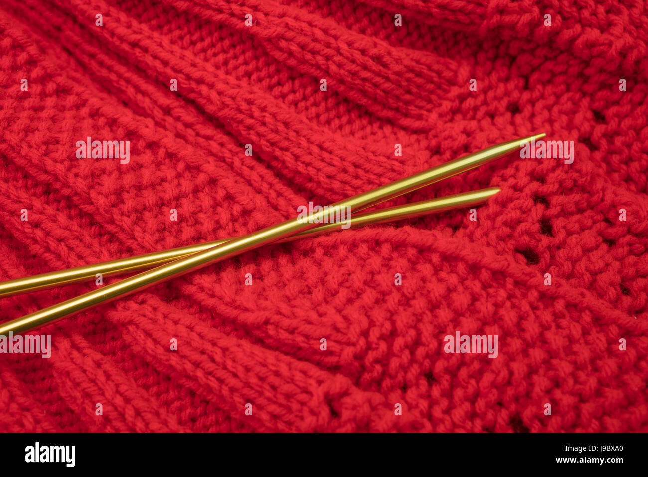 Knitted garment in red yarn and golden knitting needles on surface