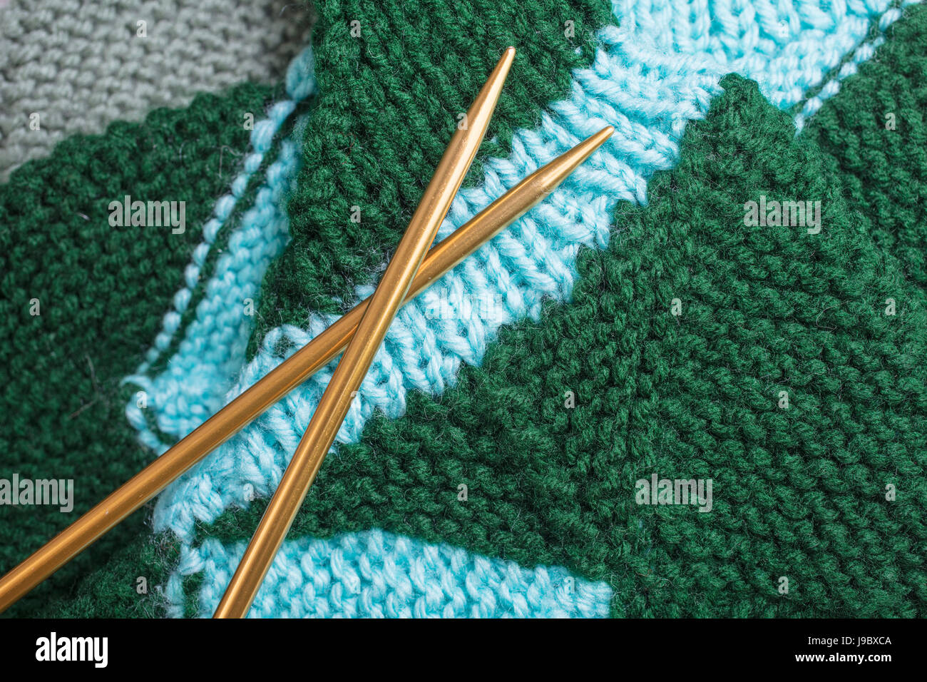 Green and teal yarn knitted socks with gold metal needles Stock Photo
