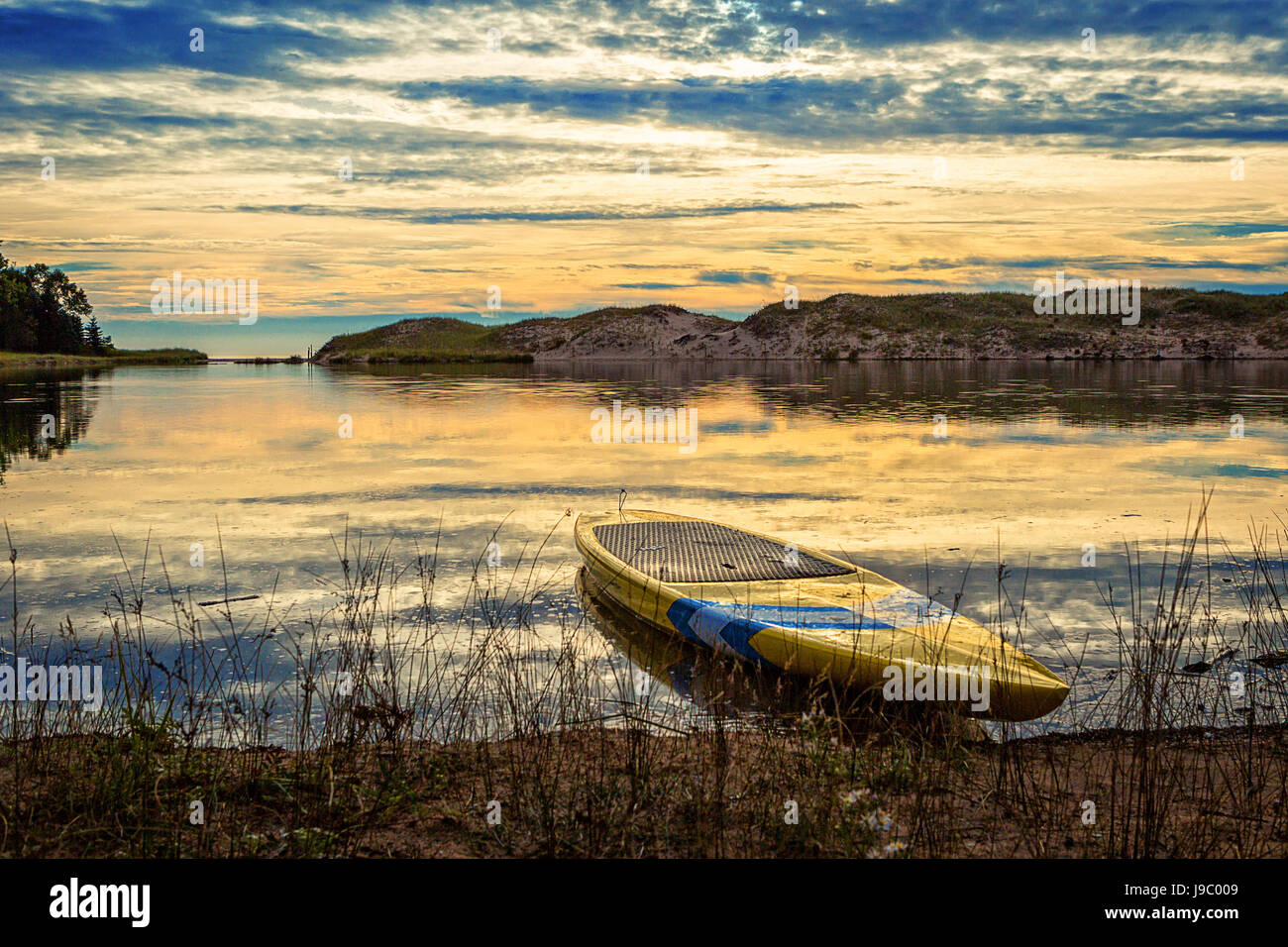 Blue and Yellow paddle board at the edge of the water North Bar Beach near Lake Michigan, Northern Michigan USA Stock Photo