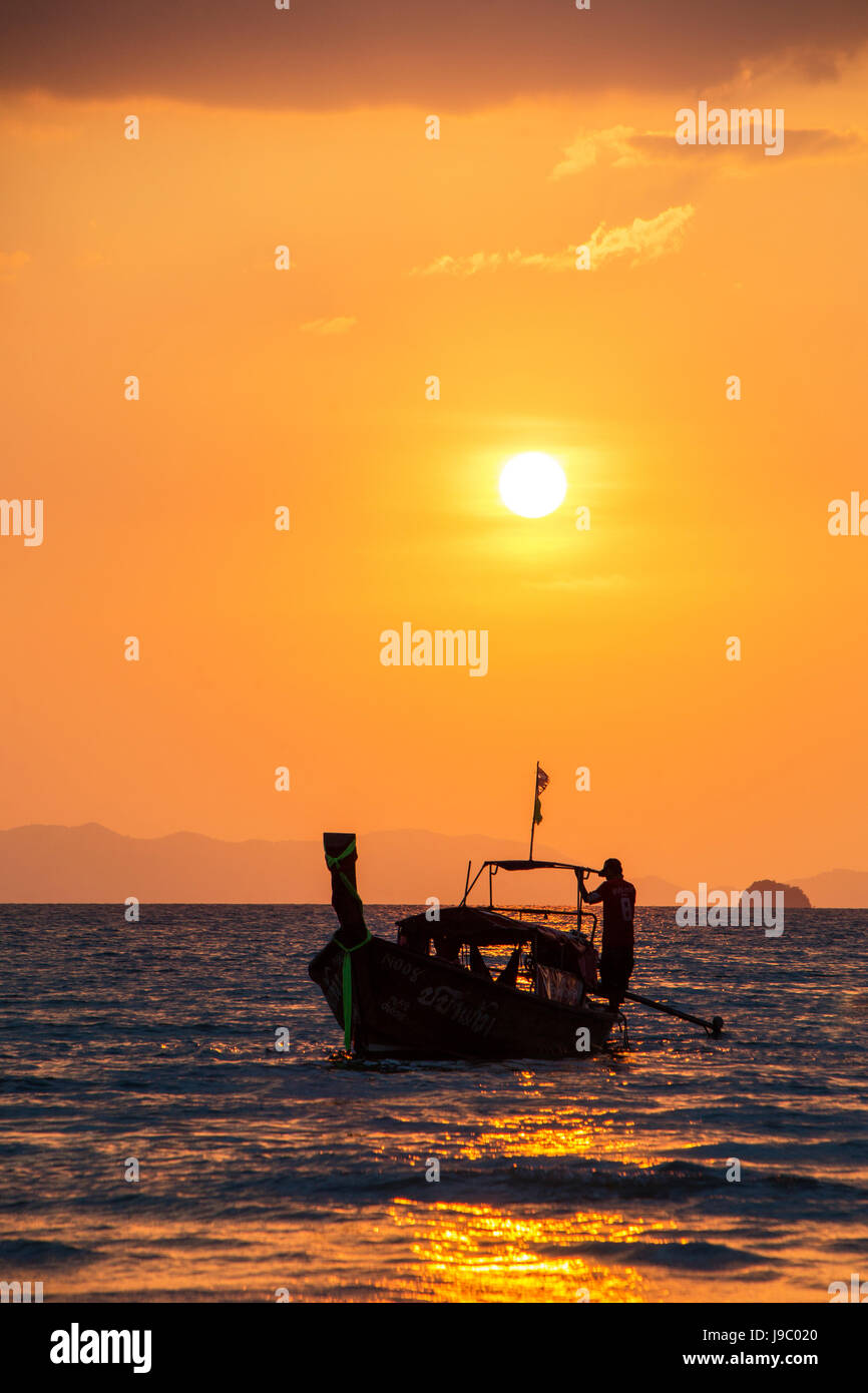 silhouette of a fisherman on a long boat at sunset off Railay Beach Thailand Stock Photo