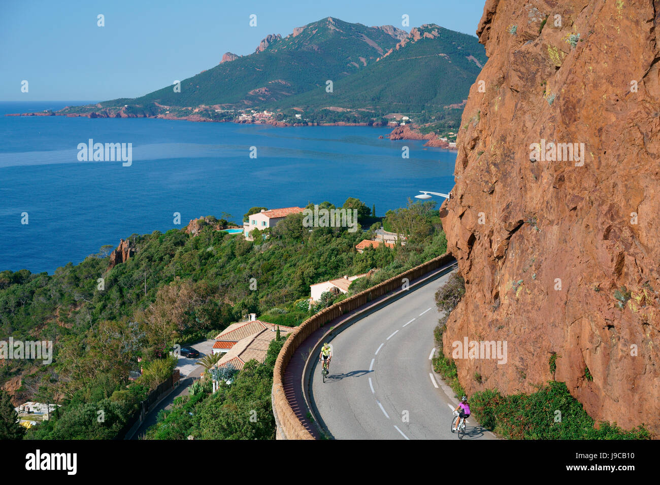 Cyclists on the scenic Corniche d'Or between the red volcanic rock of the Esterel Massif and the azure Mediterranean Sea. French Riviera, France. Stock Photo