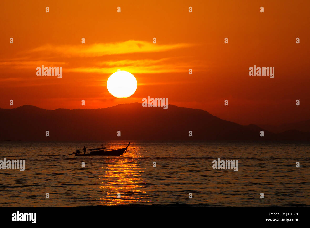 sunset at Railay Beach Krabi Province Thailand with a long boat silhouette and a large round sun setting Stock Photo